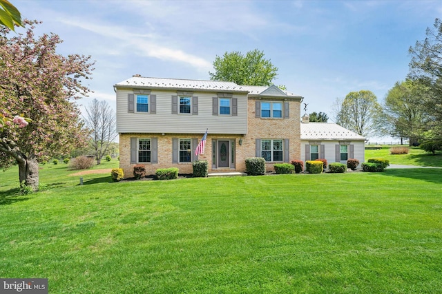 colonial home featuring brick siding, a front lawn, and metal roof