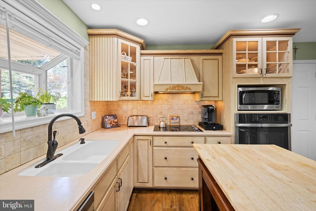 kitchen with light brown cabinetry, dark wood-style flooring, a sink, custom exhaust hood, and black appliances