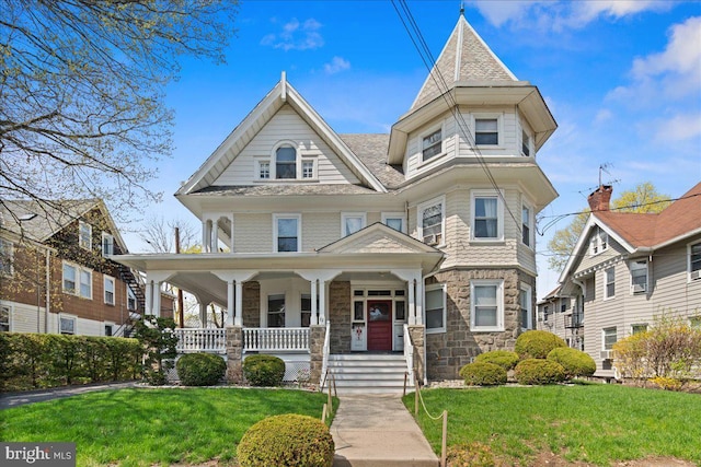 victorian-style house with a porch, a front lawn, and stone siding