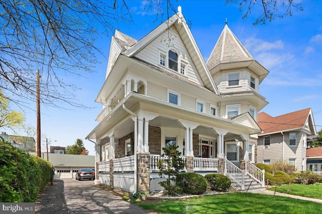victorian-style house featuring covered porch, stone siding, and a detached garage