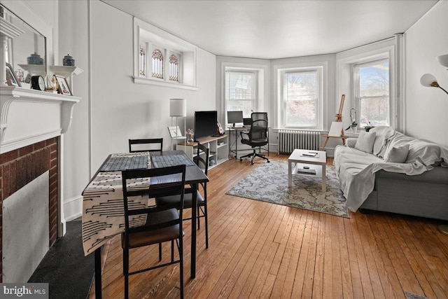 living area featuring a brick fireplace, radiator heating unit, and hardwood / wood-style flooring
