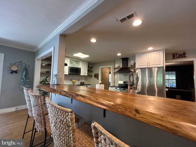 kitchen featuring visible vents, crown molding, a breakfast bar area, wood counters, and stainless steel appliances