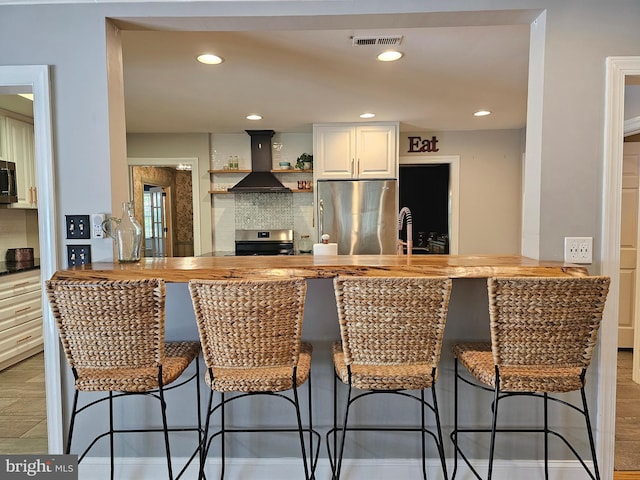 kitchen with a kitchen breakfast bar, visible vents, appliances with stainless steel finishes, a peninsula, and custom range hood