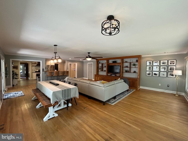 living area with crown molding, a ceiling fan, baseboards, and wood finished floors