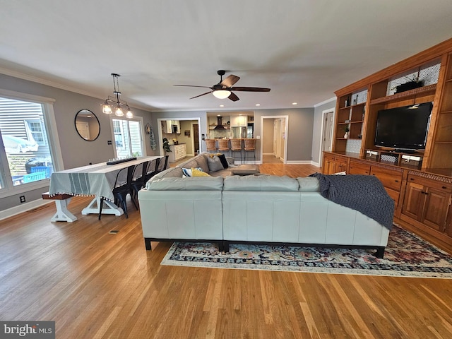 living area featuring a ceiling fan, baseboards, ornamental molding, and light wood-style flooring
