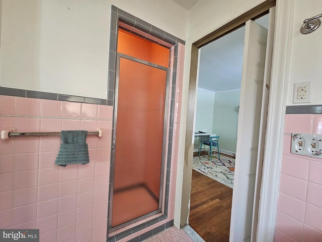 bathroom with tile walls, a shower stall, and wood finished floors
