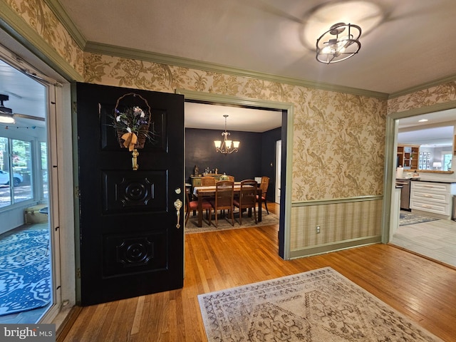 foyer entrance with crown molding, wallpapered walls, an inviting chandelier, and wood finished floors