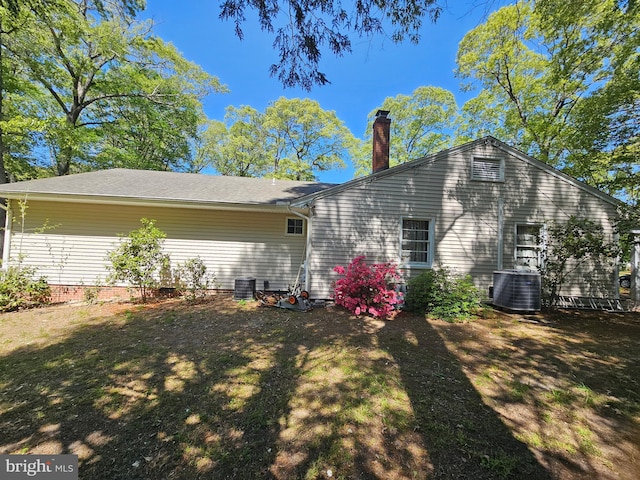 rear view of house with central air condition unit and a chimney