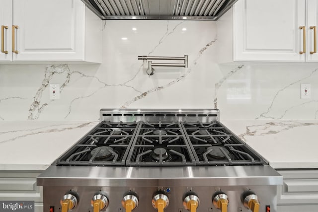 room details with wall chimney range hood, gas stove, tasteful backsplash, and white cabinetry