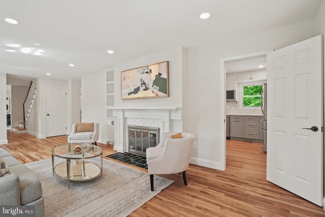 living area with stairs, a brick fireplace, light wood-style floors, baseboards, and recessed lighting