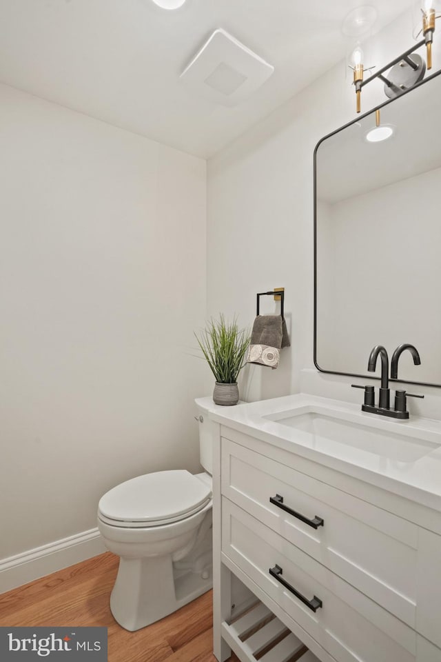 half bath featuring toilet, baseboards, wood finished floors, and vanity