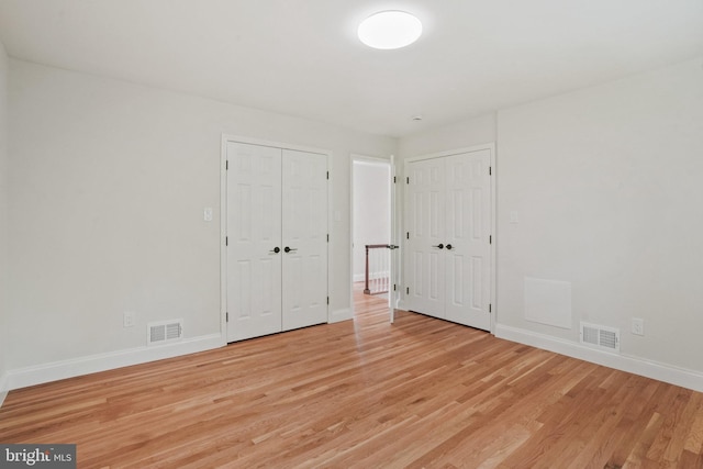unfurnished bedroom with visible vents, multiple closets, baseboards, and light wood-type flooring