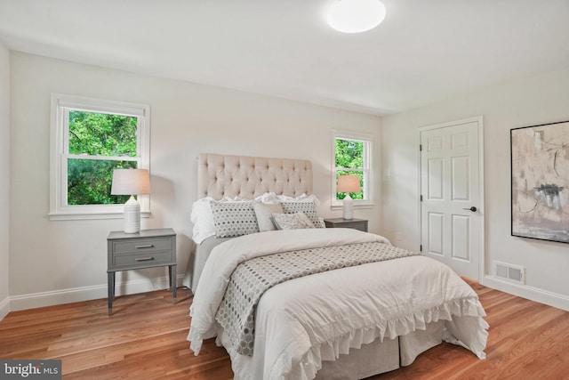bedroom with baseboards, visible vents, and wood finished floors