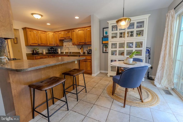 kitchen with a breakfast bar, light tile patterned floors, brown cabinets, dark countertops, and visible vents