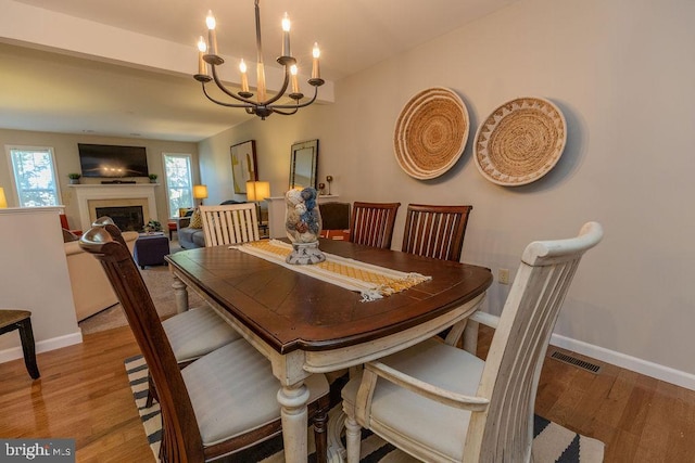 dining area with wood finished floors, a chandelier, a fireplace, baseboards, and visible vents