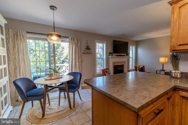 kitchen with light tile patterned floors, brown cabinetry, a glass covered fireplace, decorative light fixtures, and a peninsula