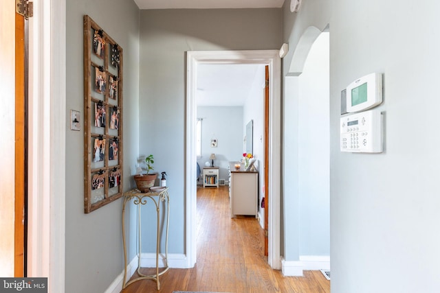 corridor with arched walkways, baseboards, and light wood-style floors