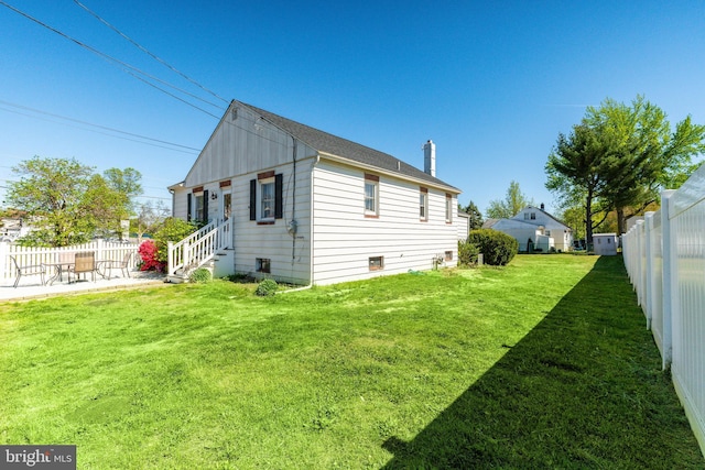rear view of property with a patio, a fenced backyard, a yard, and a chimney