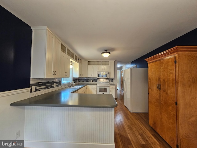 kitchen featuring white appliances, a sink, decorative backsplash, a peninsula, and dark wood finished floors
