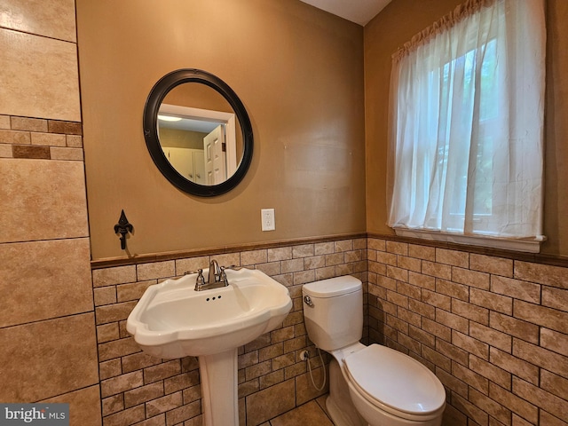 bathroom with tile walls, healthy amount of natural light, toilet, and a wainscoted wall