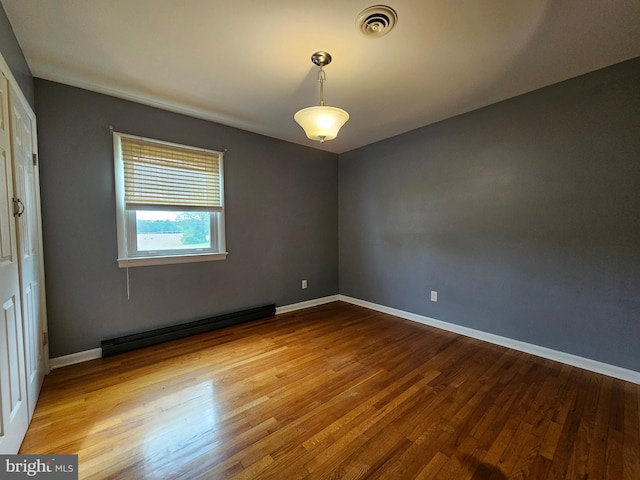 spare room featuring wood finished floors, baseboard heating, and baseboards