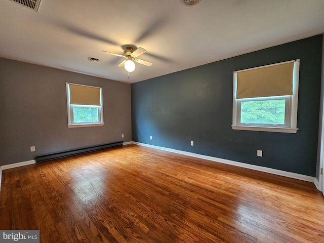 spare room featuring a baseboard heating unit, healthy amount of natural light, a ceiling fan, and wood finished floors