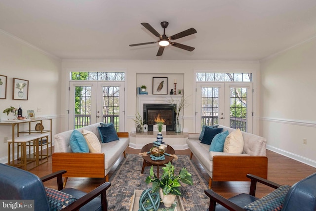 living area featuring crown molding, ceiling fan, french doors, a healthy amount of sunlight, and wood finished floors
