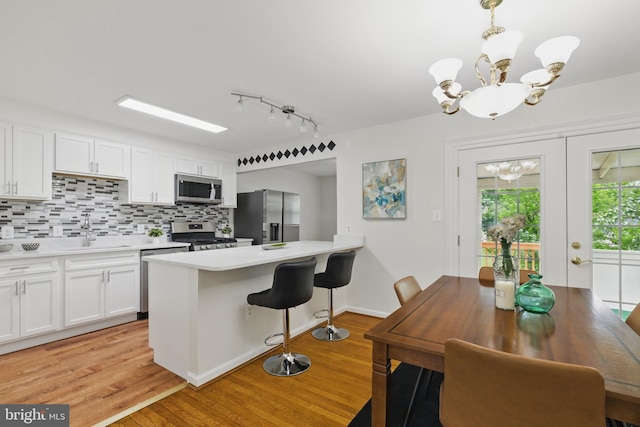 kitchen with appliances with stainless steel finishes, a sink, a chandelier, light wood-style flooring, and white cabinets