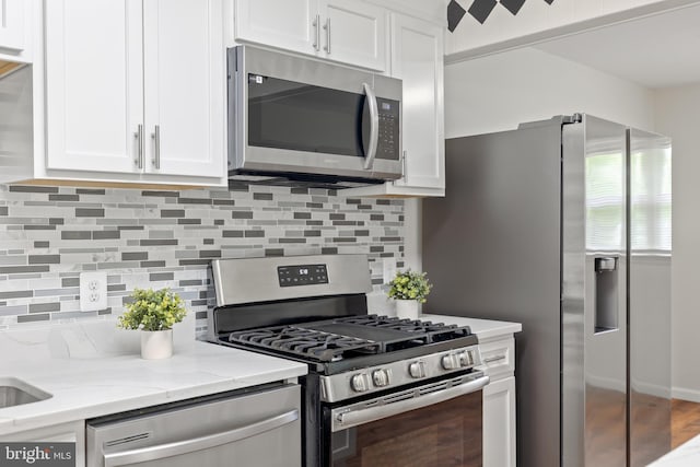 kitchen featuring stainless steel appliances, white cabinets, tasteful backsplash, and light stone countertops
