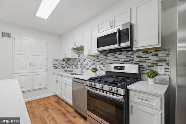 kitchen with stainless steel appliances, a sink, light countertops, and white cabinets