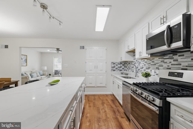 kitchen with appliances with stainless steel finishes, a sink, white cabinets, tasteful backsplash, and light wood-style floors