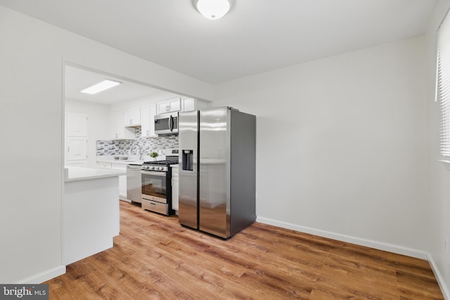 kitchen featuring appliances with stainless steel finishes, backsplash, light wood-style floors, light countertops, and white cabinets