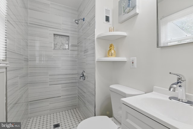 full bathroom with toilet, a tile shower, and vanity