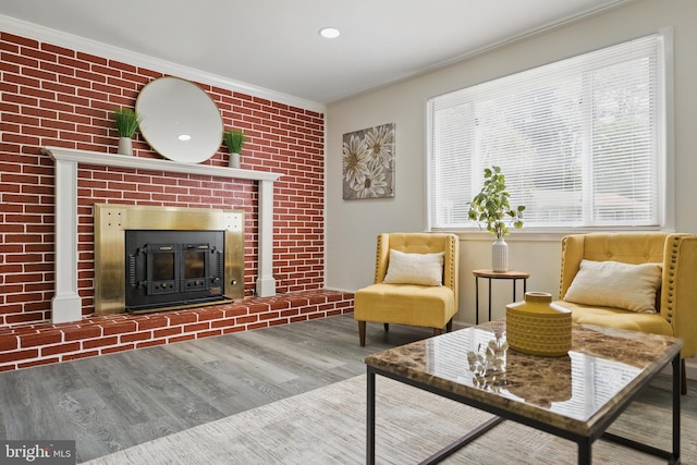 living area with ornamental molding, wood finished floors, and a brick fireplace
