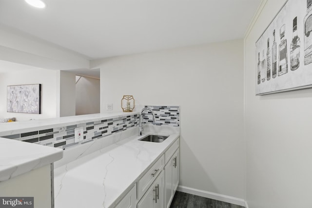 kitchen with a sink, decorative backsplash, light stone counters, dark wood-style flooring, and baseboards