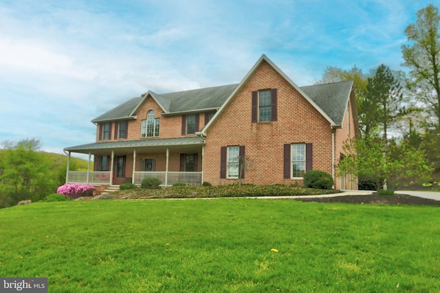 view of front facade with covered porch, a front yard, brick siding, and a standing seam roof