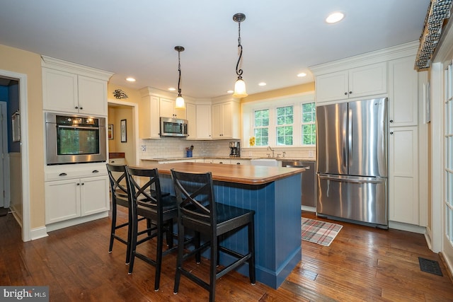kitchen with a sink, white cabinets, dark wood finished floors, appliances with stainless steel finishes, and tasteful backsplash