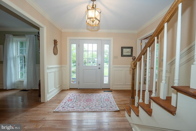 entryway featuring light wood finished floors, a wainscoted wall, a wealth of natural light, and stairs
