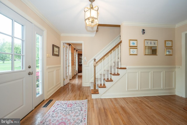 entryway featuring light wood finished floors, visible vents, a decorative wall, crown molding, and stairway