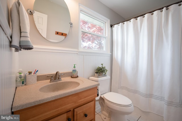 full bathroom with a wainscoted wall, a shower with shower curtain, toilet, tile patterned floors, and vanity