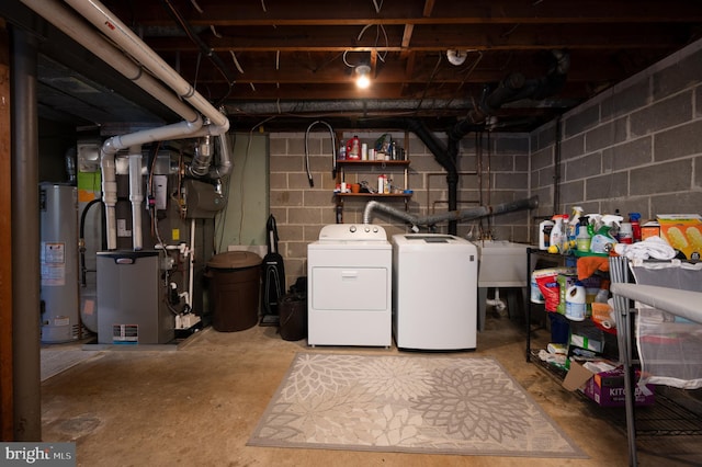 washroom with laundry area, concrete block wall, gas water heater, a sink, and washing machine and dryer
