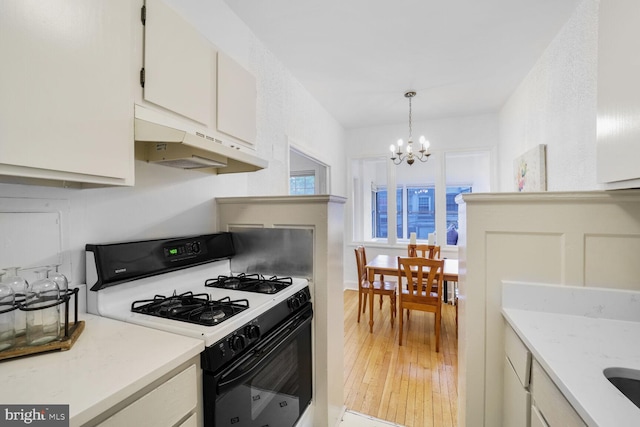 kitchen with white cabinets, an inviting chandelier, light wood-style flooring, under cabinet range hood, and gas range oven