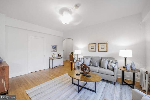 living area featuring wood-type flooring, arched walkways, baseboards, and radiator heating unit