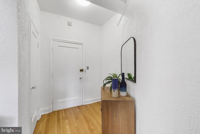 doorway to outside with baseboards, a textured wall, and light wood-type flooring