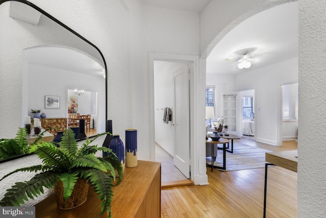 hall with arched walkways, a textured wall, baseboards, and light wood-type flooring