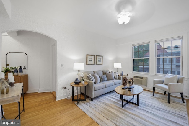 living room with light wood-style floors, arched walkways, baseboards, and a wall unit AC