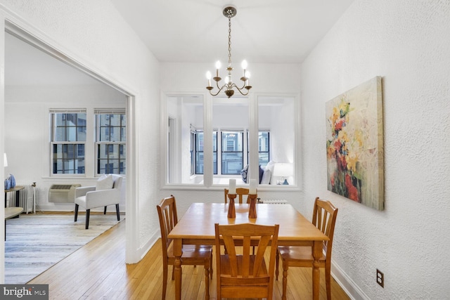 dining room with a textured wall, a notable chandelier, baseboards, light wood-type flooring, and a wall mounted AC