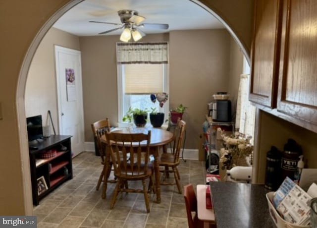 dining room with arched walkways, ceiling fan, baseboards, and light stone finish flooring