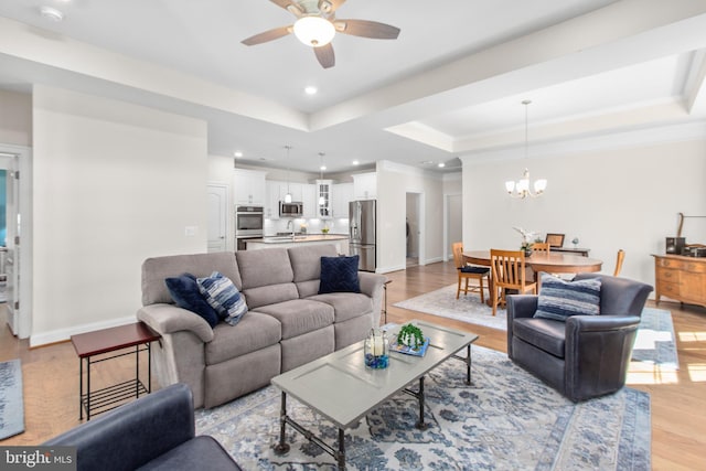 living area with a tray ceiling, ceiling fan with notable chandelier, and light wood-style floors