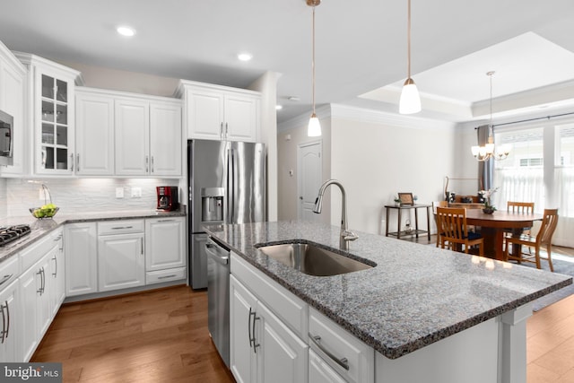 kitchen with crown molding, a sink, white cabinets, stainless steel appliances, and an island with sink
